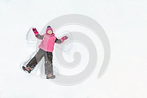 Cute little kid girl in warm ski sport suit making snow angel outdoors. Kid having fun lying on snowdrift after snow