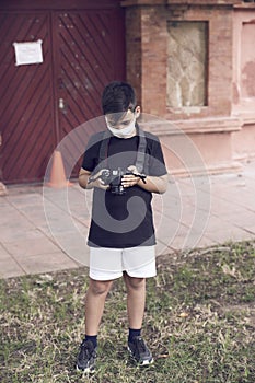 A cute little kid with green eyes wearing a mask is holding a camera and taking pictures . Happy boy dreams of becoming