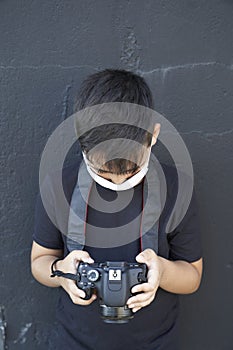 A cute little kid with green eyes wearing a mask is holding a camera and taking pictures . Happy boy dreams of becoming