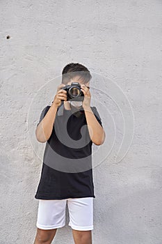 A cute little kid with green eyes wearing a mask is holding a camera and taking pictures . Happy boy dreams of becoming