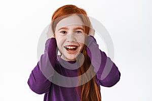Cute little kid with red hair shut her ears and smiling, acting childish, unwilling to listen, misbehave, laughing and photo
