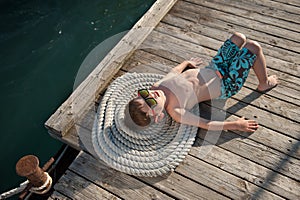 Cute little kid sunbathing lying on rope and wooden pier