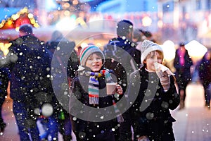 Cute little kids girl and boy having fun on traditional Christmas market during strong snowfall. Happy children eating