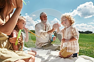 Cute little kids having fun while spending time with their parents, family having picnic in nature on a summer day