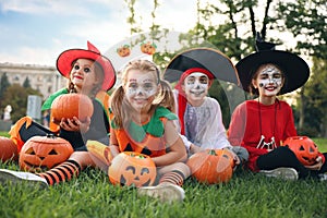 Cute little kids with pumpkins wearing Halloween costumes in park