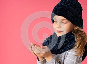 Cute little lady in a warm hat and scarf, having something in her hands, enjoying a miracle on a pink background.