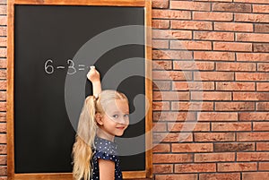 Cute little left-handed girl doing sums on chalkboard