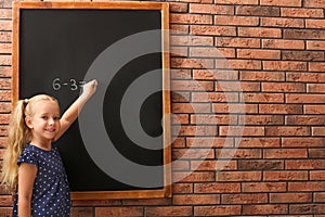 Cute little left-handed girl doing sums on chalkboard near  wall