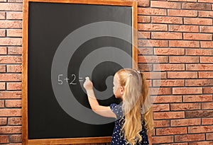 Cute little left-handed girl doing sums on chalkboard near wall