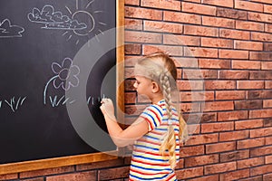 Cute little left-handed girl drawing on chalkboard near wall