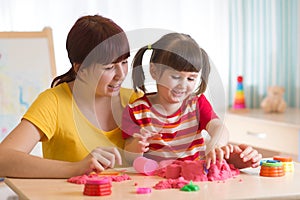 A cute little little girl and her mom playing with kinetic sand at home