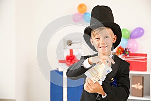 Cute little magician showing trick with money indoors