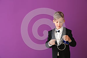 Cute little magician showing trick with rings on color background