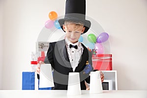 Cute little magician showing tricks with cups indoors