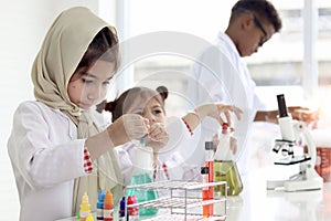 Cute little Muslim girls in lab coat wearing hijab scarf and doing experiment together with her friend, young scientist kid