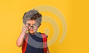 Cute little nerd smart boy wearing glasses isolated on yellow background. Funny pupil with red big backpack ready to go