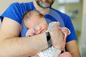 Cute little newborn baby boy in his fathers arms. Portrait of tiny new baby at home. Adorable son being held by his daddy