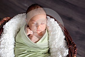 Cute little newborn baby boy, sleeping in basket with wrap