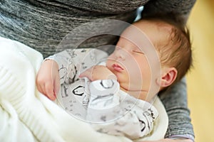 Cute little newborn baby boy sleeping in his mothers arms. Portrait of tiny new baby at home. Adorable son being held by his mommy