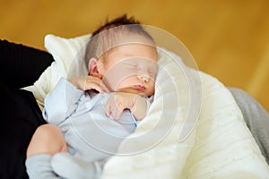 Cute little newborn baby boy sleeping in his mothers arms. Portrait of tiny new baby at home. Adorable son being held by his mommy