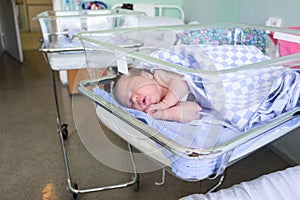 Cute little newborn baby sleeping in infant bed in hospital, folded hands with open mouth