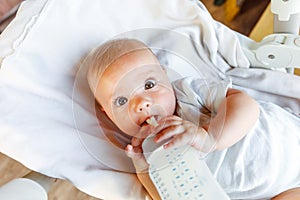 Cute little newborn girl drinking milk from bottle and looking at camera on white background. Infant baby sucking eating
