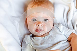 Cute little newborn girl with smiling face looking at camera on white background. Infant baby resting playing lying down