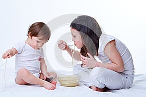 Cute little playful sisters eating yummy pasta in white studio background