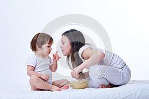 Cute little playful sisters eating yummy pasta in white studio background