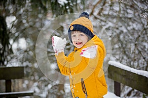 Cute little preschool boy, playing outdoors with snow on a winter day