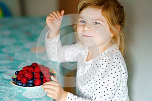 Cute little preschool girl eating fresh raspberries and blueberries. Happy child tasting raspberry and blueberry