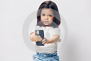 a cute little preschool girl stands on a white background in a white T-shirt and takes pictures of herself on her