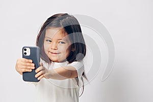 a cute little preschool girl stands on a white background in a white T-shirt and takes pictures of herself on her