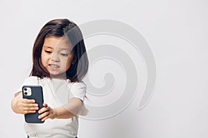 a cute little preschool girl stands on a white background in a white T-shirt and takes pictures of herself on her