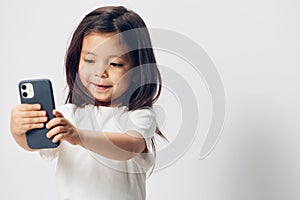 a cute little preschool girl stands on a white background in a white T-shirt and takes pictures of herself on her