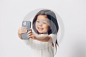 a cute little preschool girl stands on a white background in a white T-shirt and takes pictures of herself on her