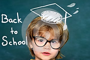 Cute little preschool kid boy in a classroom. Blackboard background. Teachers day. Kids from primary school. September 1