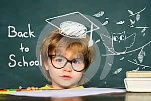 Cute little preschool kid boy in a classroom. Blackboard background. Teachers day. Kids from primary school. September 1