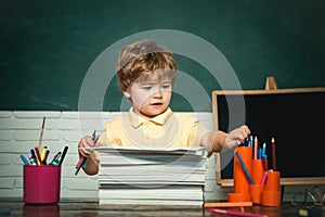 Cute little preschool kid boy study in a classroom. Funny little kid pointing up on blackboard - school concept. Kid is