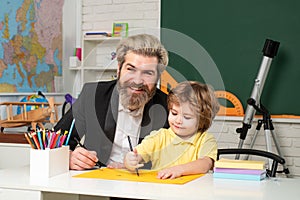 Cute little preschool kid boy with teacher study in a classroom. Teacher and pupil in classroom.