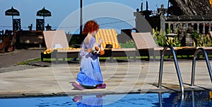 Cute little redhead girl in her daddy's t-shirt walks along the pool
