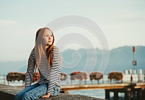 Cute little redheaded girl resting by lake Geneva at sunset