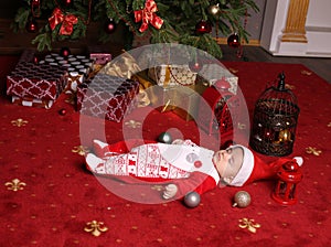 Cute little Santa baby sleeping beside Christmas tree with a lot of presents