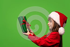 Cute little Santa girl in a hat holds a New Year's gift in her hands and looks at him. Happy New Year. Isolated on