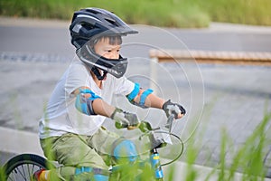 Cute little school boy child in safety helmet wearing knee pads, elbow pads and cycling gloves riding a bike on nature