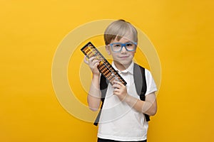 Cute little school boy in glasses holding abacus on yellow background. Mental arithmetic