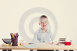 Cute little school boy with huge smile sitting at his desk on white background. Happy intelligent children in shirt