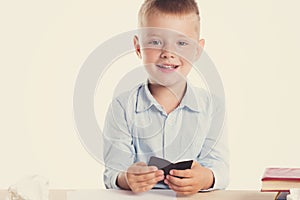 Cute little school boy with huge smile sitting at his desk on white background. Happy intelligent children in shirt with blue eyes