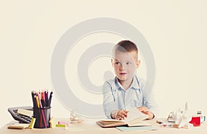 Cute little school boy with huge smile sitting at his desk on white background. Happy intelligent children in shirt with blue eyes