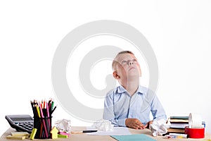 Cute little school boy with sad face sitting at his desk on whit